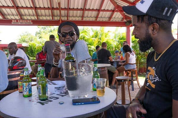 Two men sit at a table that has a bottle of rum in an ice bucket on top of it, along with several bottles of Deputy beer.